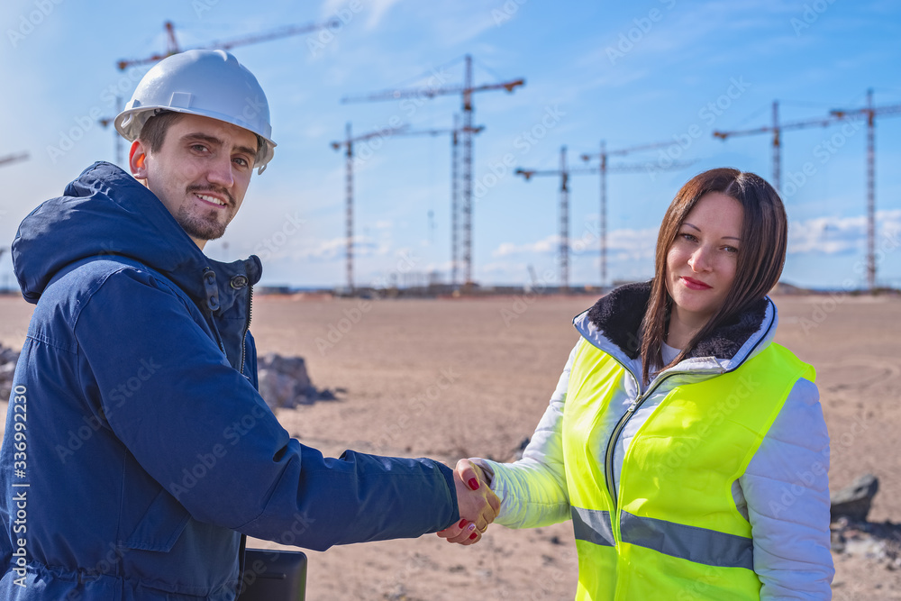 a Builder and a real estate agent shake hands in front of a building under construction a Builder and a real estate agent shake hands in front of a building under construction