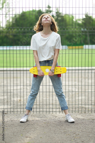 Redhead white girl with skateboard near fence