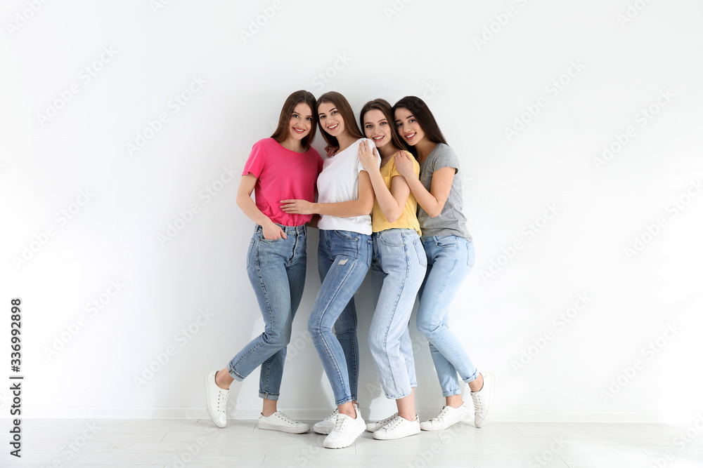 Beautiful young ladies in jeans and colorful t-shirts near white wall indoors. Woman's Day Beautiful young ladies in jeans and colorful t-shirts near white wall indoors. Woman's Day
