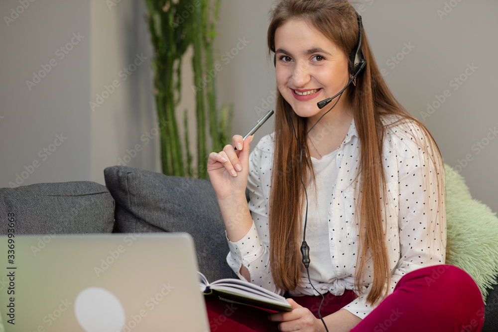Happy girl e-learning with laptop and headphones sitting on a couch in the living room at home Happy girl e-learning with laptop and headphones sitting on a couch in the living room at home