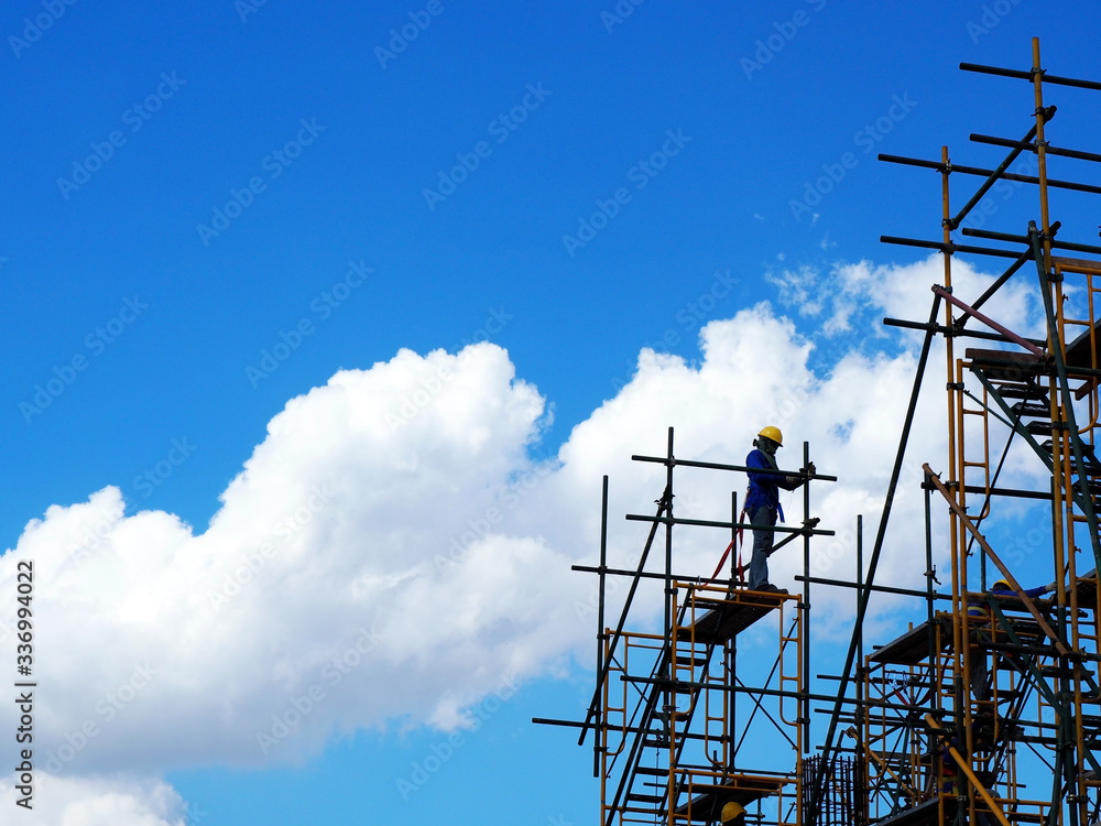 Construction workers working on scaffolding, Man Working on the Working at height with blue sky at construction site Construction workers working on scaffolding, Man Working on the Working at height with blue sky at construction site