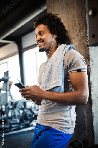 Young handsome man using phone while having exercise break in gym