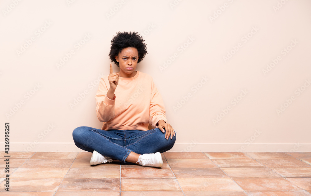 African american woman sitting on the floor frustrated and pointing to the front