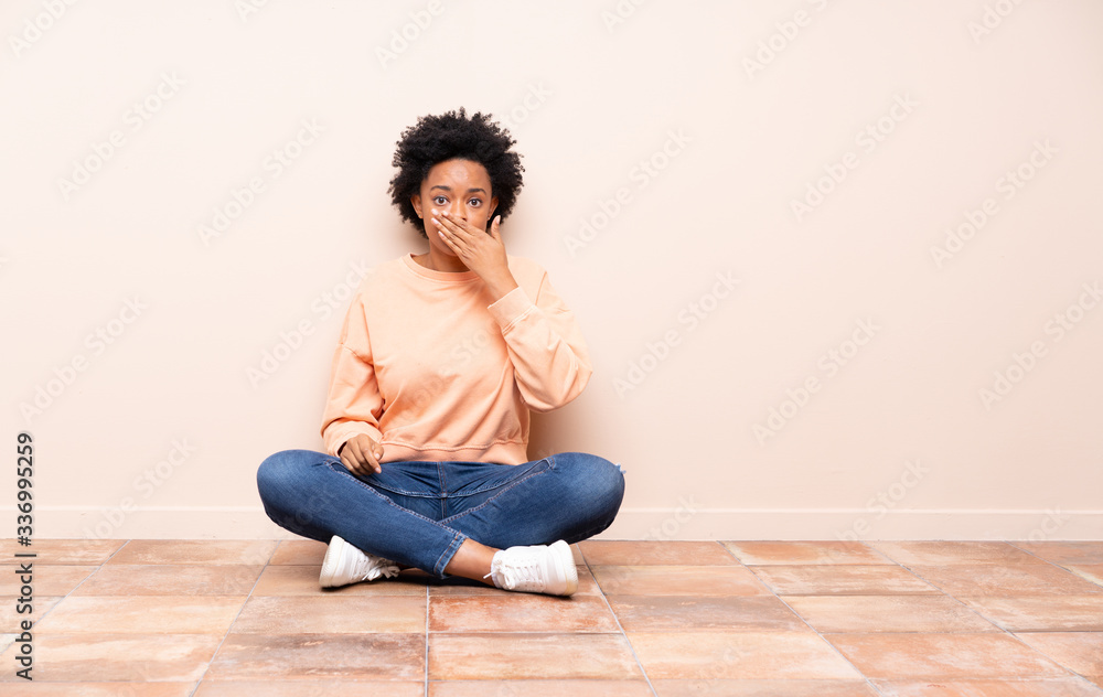 African american woman sitting on the floor covering mouth with hands African american woman sitting on the floor covering mouth with hands