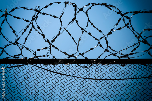 Silhouette of a fence with barbed wire against the blue sky.