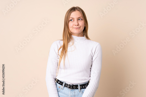 Teenager Ukrainian girl isolated on beige background having doubts while looking up