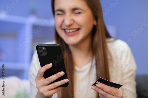 Cheerful female using mobile phone while doing online payment with bank card on purple background.