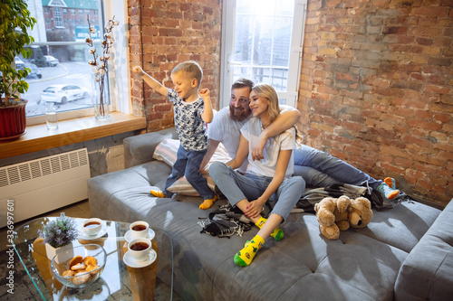Mother, father and son at home having fun, comfort and cozy concept. Looks happy, cheerful and joyful. Beautiful caucasian family. Spending time together, playing, watching cinema, lying on sofa.