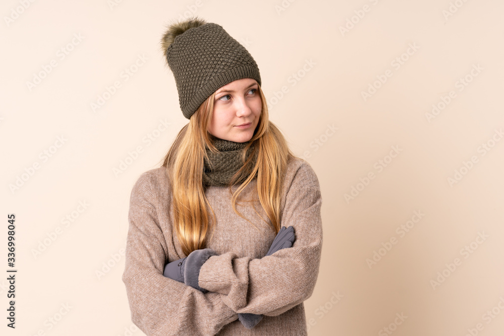 Teenager Ukrainian girl with winter hat isolated on beige background thinking an idea