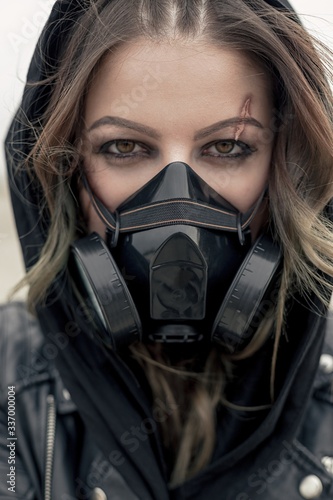 Portrait of a young woman wearing a black respirator, posing outdoors