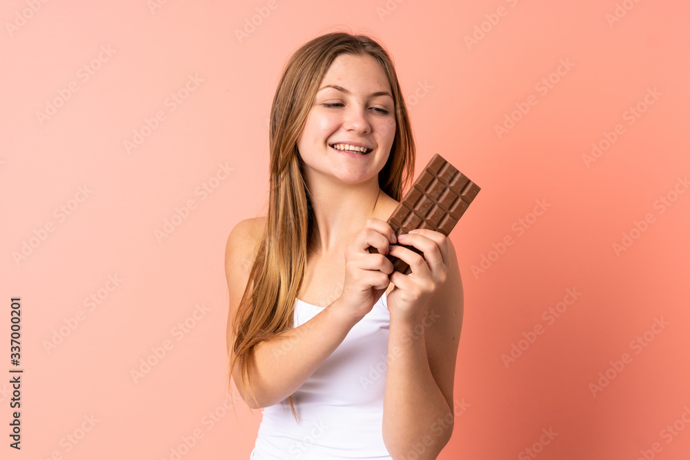 Teenager Ukrainian girl isolated on pink background taking a chocolate tablet and happy Teenager Ukrainian girl isolated on pink background taking a chocolate tablet and happy