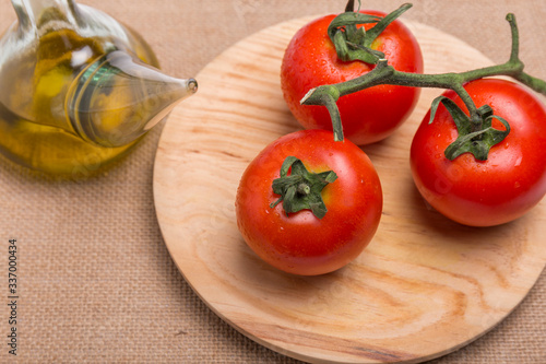 glass container with olive oil next to some red tomatoes on a wooden board, on a brown background, seen from above