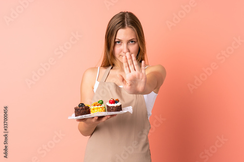 Pastry Ukrainian chef holding a muffins isolated on pink background making stop gesture with her hand