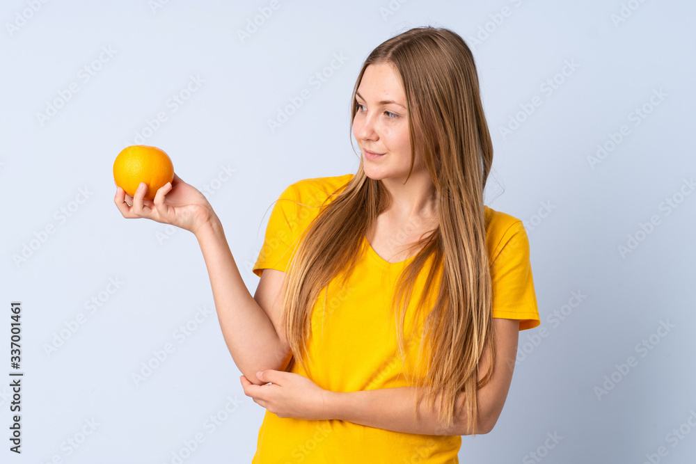 Teenager Ukrainian girl isolated on blue background holding an orange Teenager Ukrainian girl isolated on blue background holding an orange