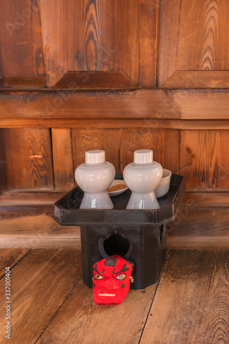 Small red mask of Tengu in front of a tray made of cypress wood topped with shinto offerings composed of sake in a two bottles, rice in a plate and water in a bowl. photo