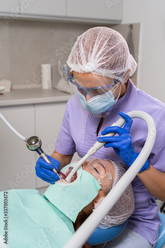 with the help of a special tool, the dentist carries out powder brushing of teeth to the patient girl