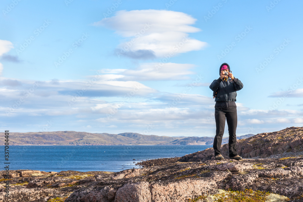 Obraz premium A middle-aged woman taking pictures standing on the rock. travel concept