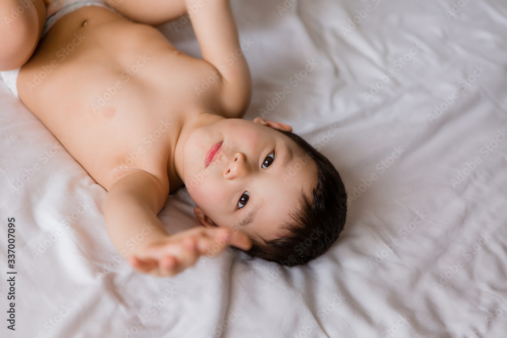 Cute toddler boy in diapers lies on bed with white sheet Cute toddler boy in diapers lies on bed with white sheet