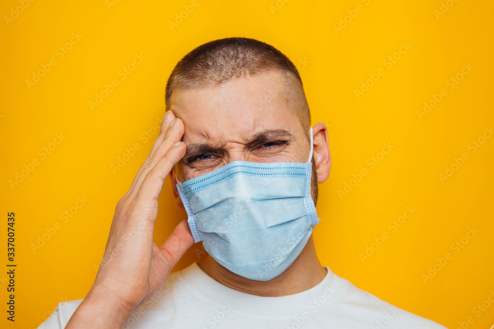 The guy holds on to his head, indicating that it hurts. Attractive man in a mask looks at the camera. Colds, flu, virus, tonsillitis, acute respiratory infections, quarantine, epidemic concept. The guy holds on to his head, indicating that it hurts. Attractive man in a mask looks at the camera. Colds, flu, virus, tonsillitis, acute respiratory infections, quarantine, epidemic concept.
