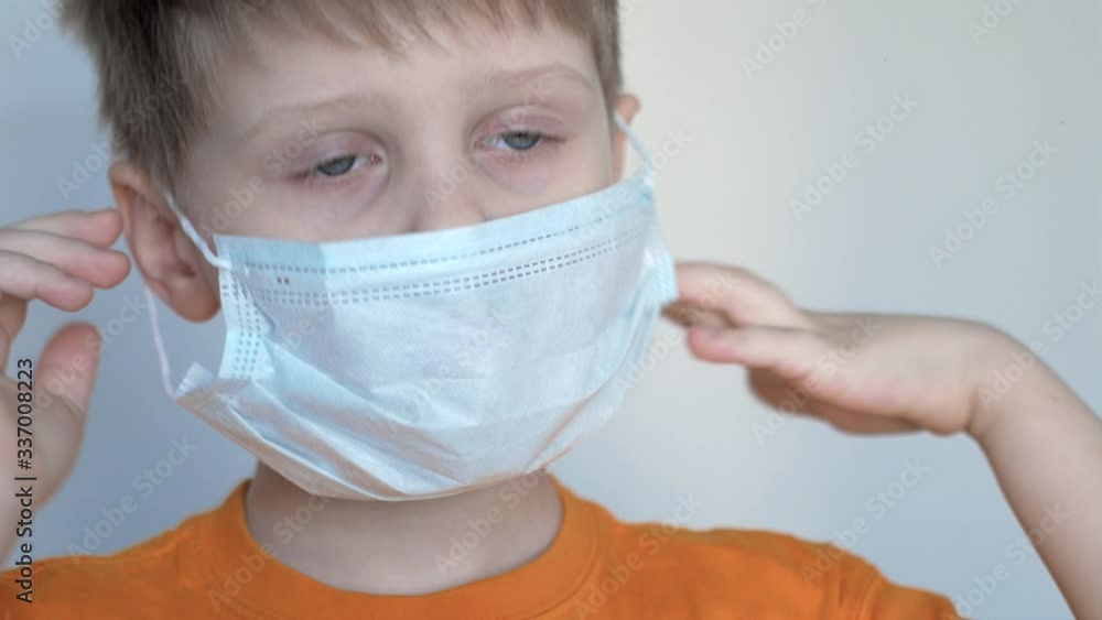 Close-up of a boy with blue eyes puts a mask on his face, on a white background and looks into the distance, he is protected from the coronavirus Close-up of a boy with blue eyes puts a mask on his face, on a white background and looks into the distance, he is protected from the coronavirus