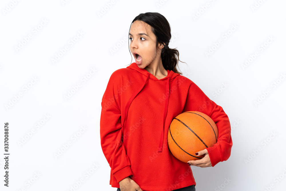 Young woman playing basketball over isolated white background doing surprise gesture while looking to the side