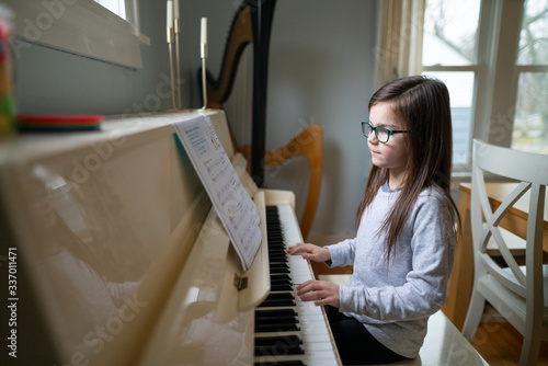 Young girl wearing glasses while reading music and practicing the piano at home photo