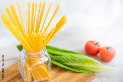 Raw Italian spaghetti in the glass jar and ingredients for cooking.