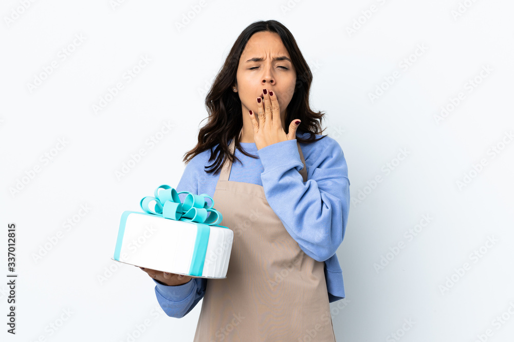 Pastry chef holding a big cake over isolated white background yawning and covering wide open mouth with hand Pastry chef holding a big cake over isolated white background yawning and covering wide open mouth with hand