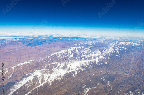 Mountains with snowy peaks from the window of an airplane on a sunny day.