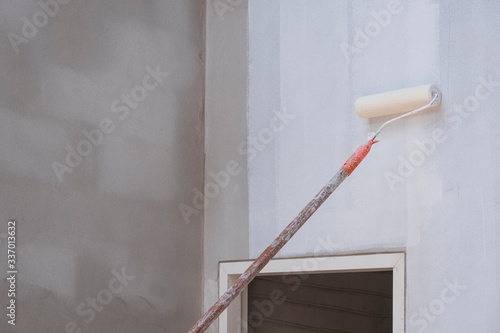 Long handle roller brush applying primer white paint with door frame on cement wall inside of house construction site, building and home renovation concept