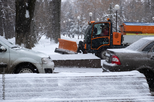 Snow plow is sprincling salt or de-icing chemicals on pavement in city. Cleaning service. Frost winter season. Winter anti-slip road handling concept.