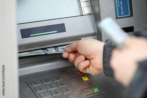 Male hands holding bunch of hundred dollars banknotes at atm machine photo