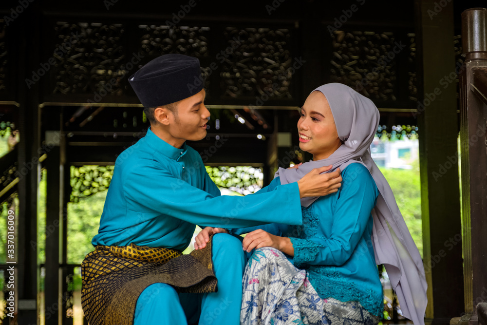 A portrait of young couple of malay muslim in traditional costume showing romantic gesture during Aidilfitri celebration.