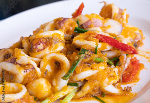 Stir fried squid with salted eggs in the white plate.