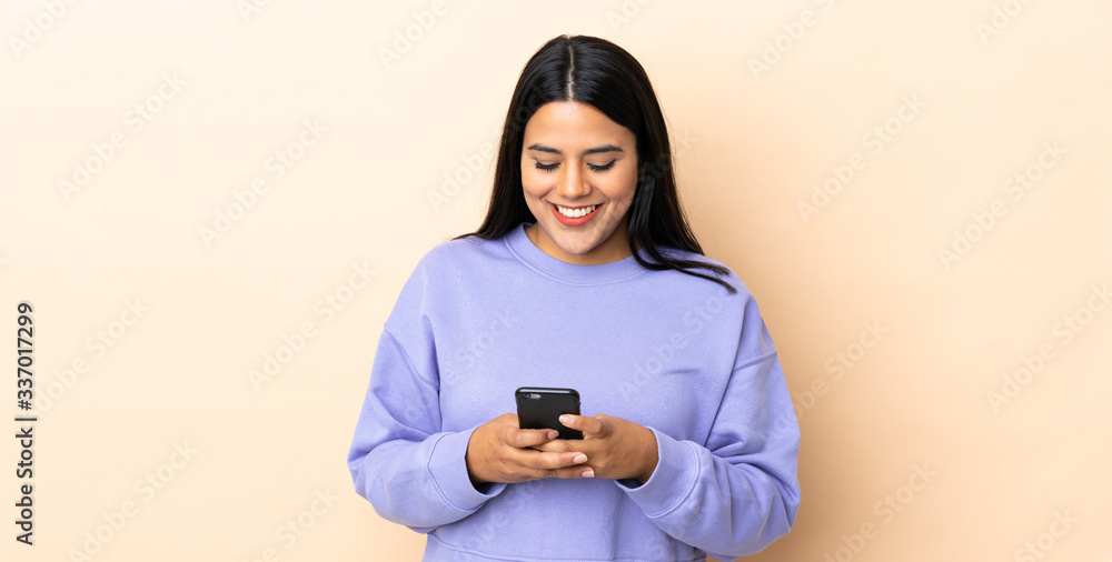 Young latin woman woman over isolated background sending a message with the mobile Young latin woman woman over isolated background sending a message with the mobile