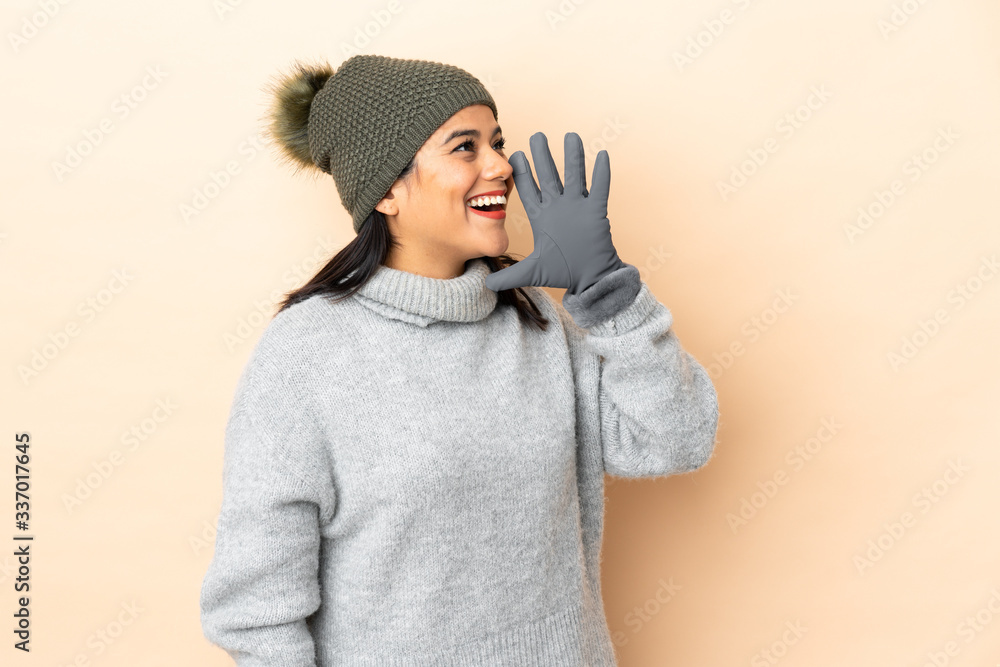 Young Colombian girl with winter hat isolated on beige background shouting with mouth wide open