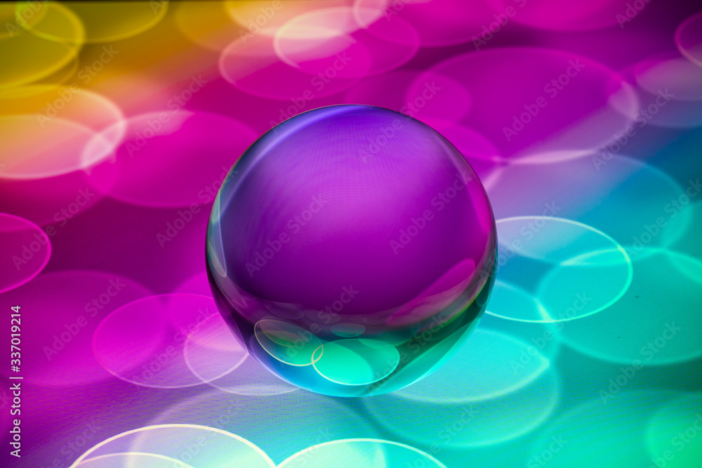 Crystal glass ball is lying on a stone surface on the colorful abstract background. Crystal glass ball is lying on a stone surface on the colorful abstract background.