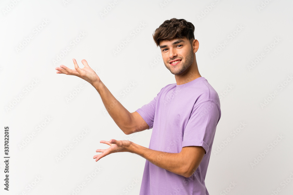 Young handsome man over isolated white background extending hands to the side for inviting to come Young handsome man over isolated white background extending hands to the side for inviting to come