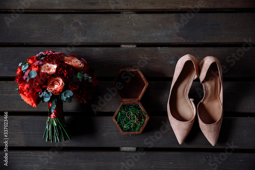 Wedding bouquet of peonies and carnations  shoes and rings  other wedding accessories on a wooden background