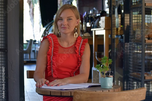 Sitting girl in a red dress reading the menu. Young girl sitting at a table in a cafe.Young beautiful girl in a cafe Marmaris    