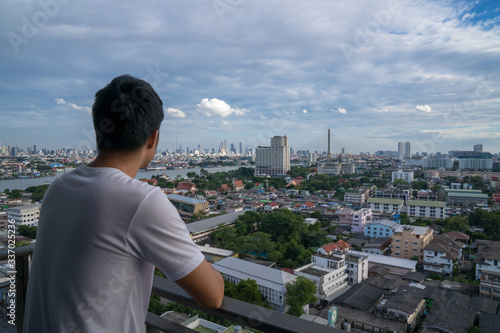Asian young man stay at home and watching cityscape  from his balcony during covid-19 situation © PordeeStudio