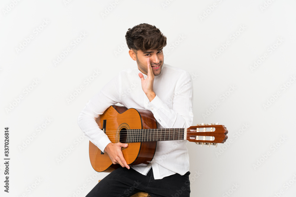 Young handsome man with guitar over isolated white background whispering something Young handsome man with guitar over isolated white background whispering something