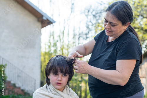 mother cuts her son's hair in the garden - at home the mother is a hairdresser for her son © Emanuele Capoferri