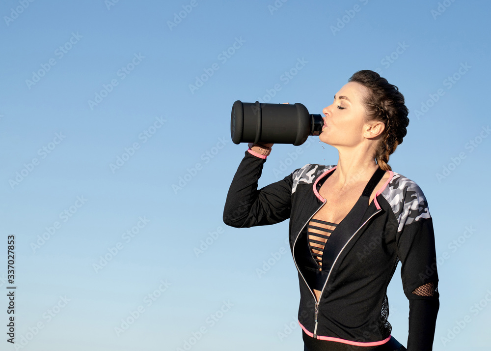 Caucasian female fitness model drinking from a water bottle during exercise outdoor isolated