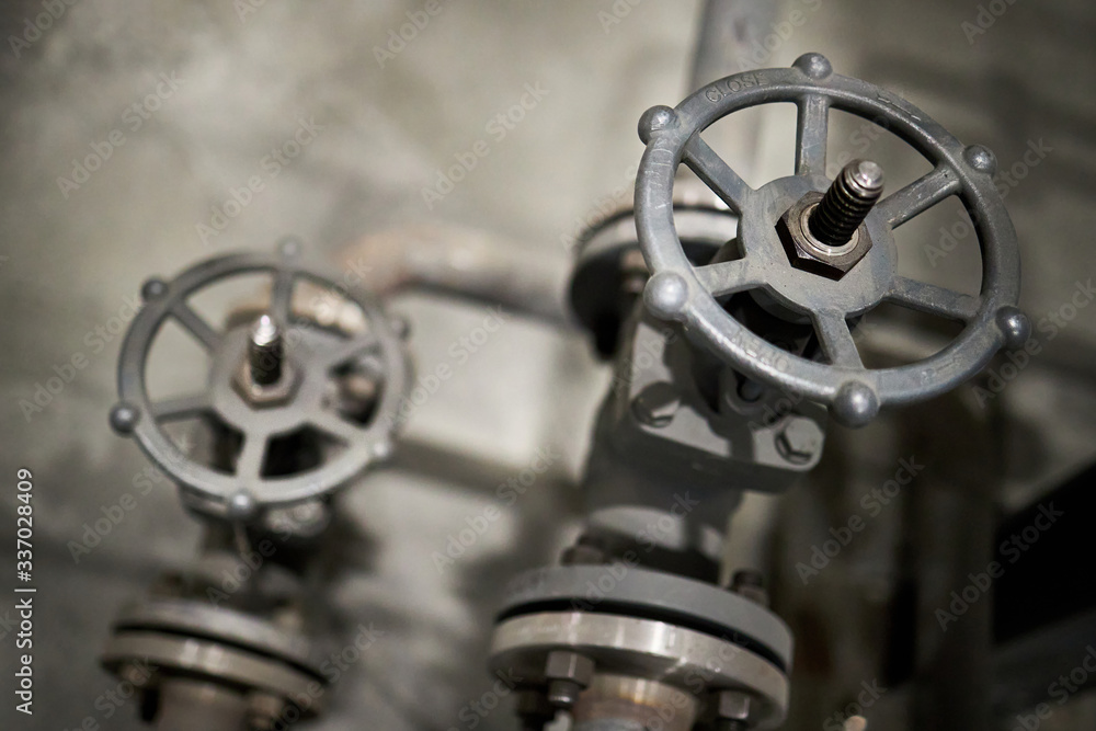 Close-up of industrial pair of valves with focus on foreground ventil with inscription open and close on helm and direction indicator arrow with copy space.