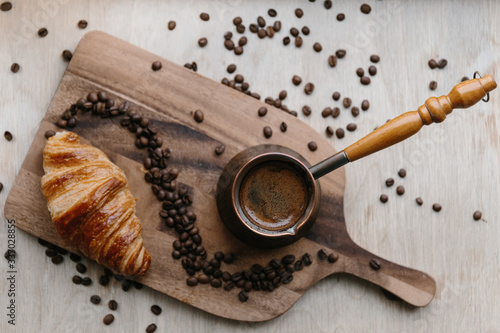 Turkish coffee pot, croissant and coffee beans on wooden board