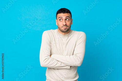 Young man over isolated blue background making doubts gesture while lifting the shoulders