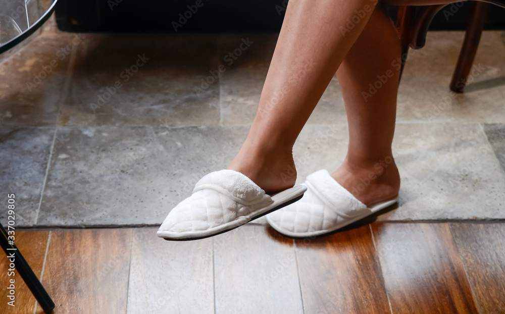 Cómoda zapatilla pantufla colocada en el pie de una mujer sentada y con las piernas cruzadas en un día relajante Cómoda zapatilla pantufla colocada en el pie de una mujer sentada y con las piernas cruzadas en un día relajante