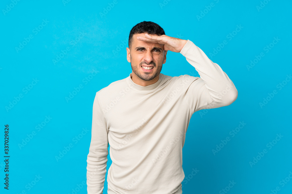 Young man over isolated blue background looking far away with hand to look something Young man over isolated blue background looking far away with hand to look something