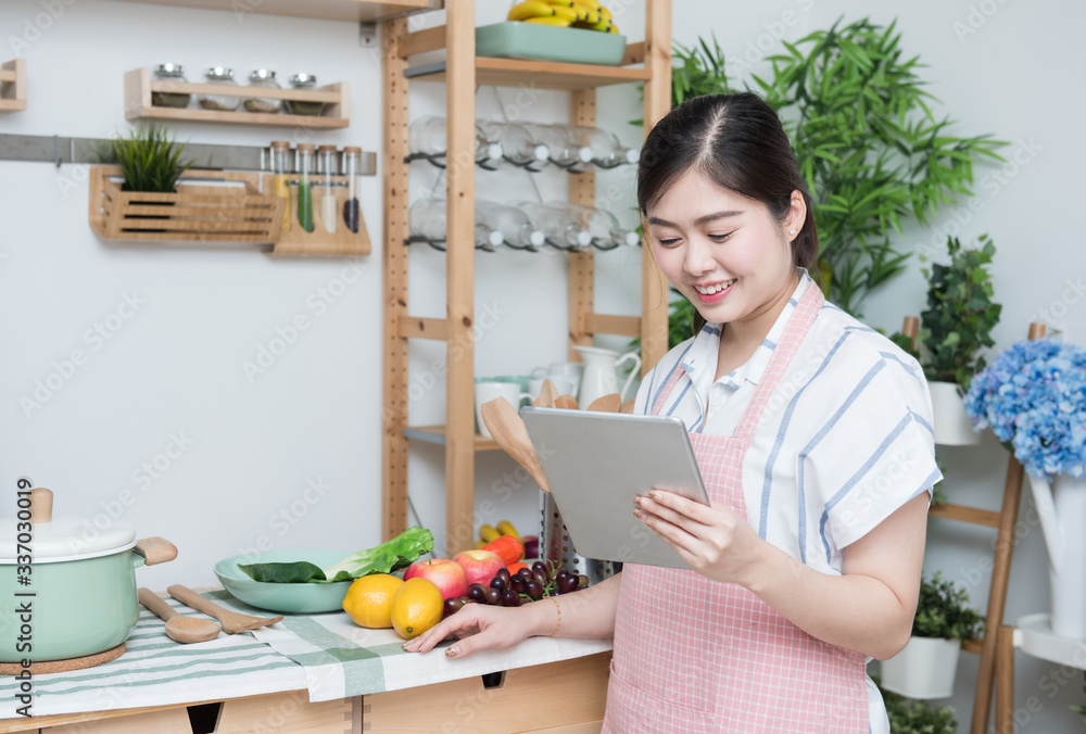 Φωτογραφία Happy asian woman looking recipe tablet kitchen reading cooking at home,University colleague student study online with social media,Social distancing, stay at home and work from home concept